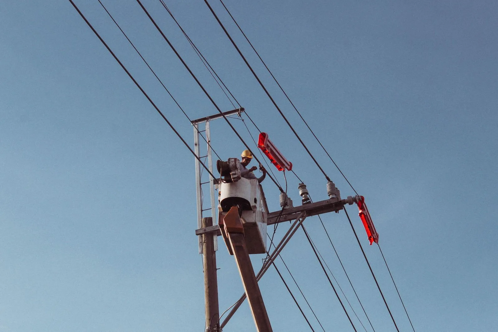 Utility worker on a hoist repairing a power line